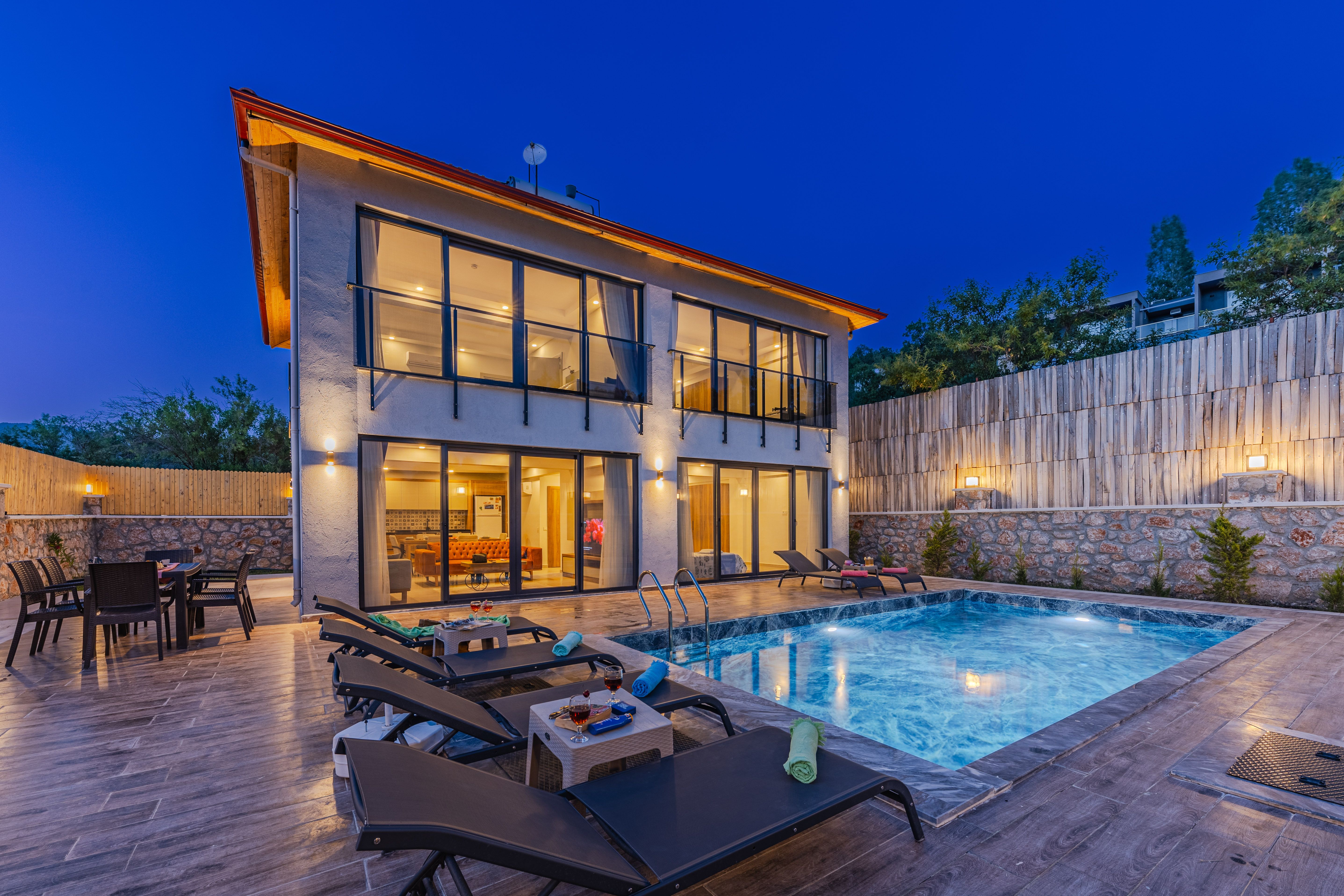 Villa contemporaine éclairée le soir avec terrasse extérieure, piscine et grandes baies vitrées.
