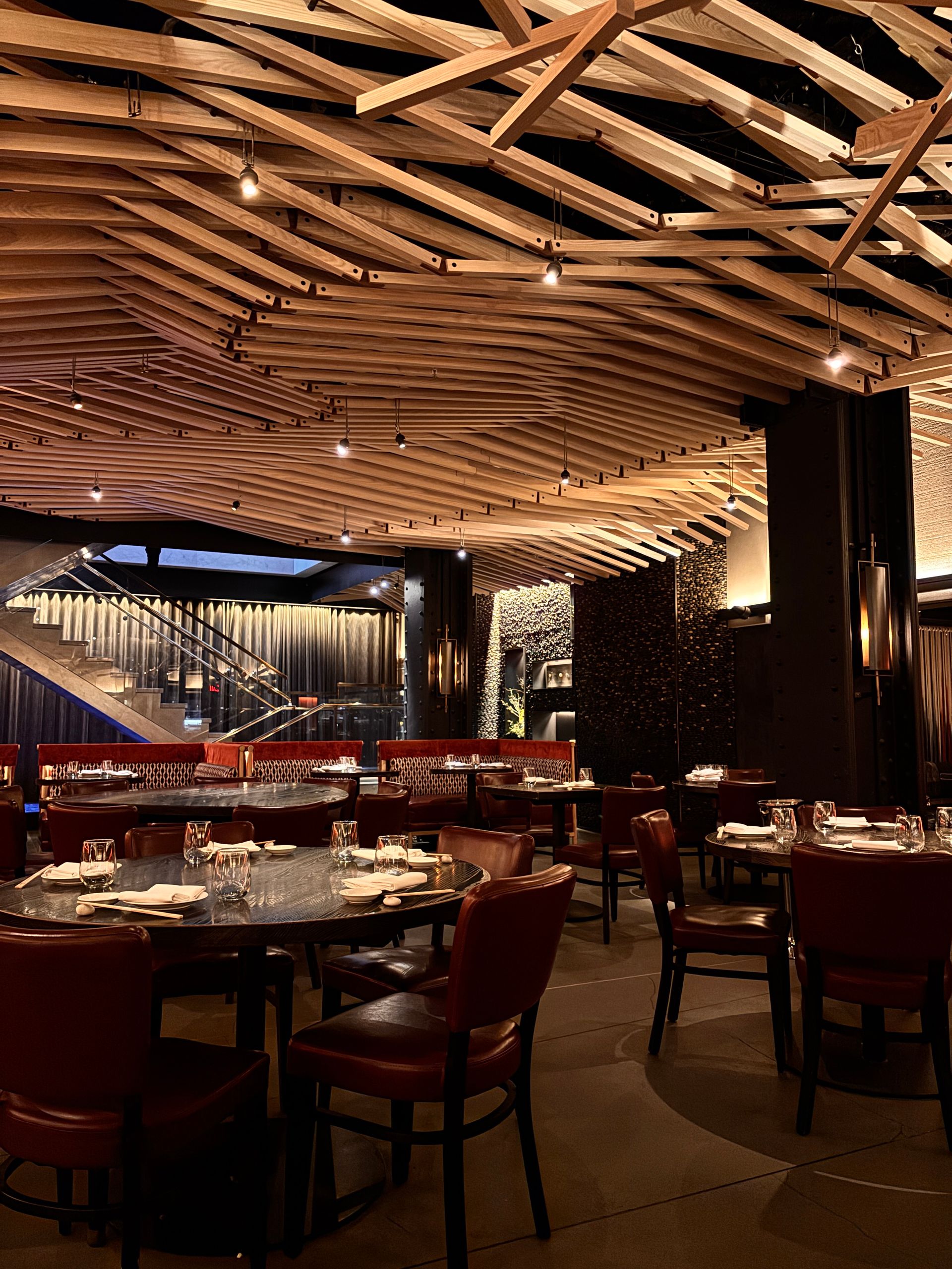 Salle de restaurant élégante avec plafond en lames de bois, tables dressées et banquettes rouges.