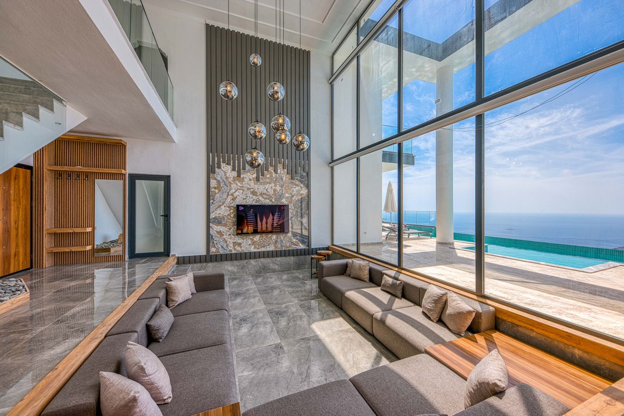 Salon contemporain ouvert sur la mer avec suspensions rondes, boiseries et larges vitrages.